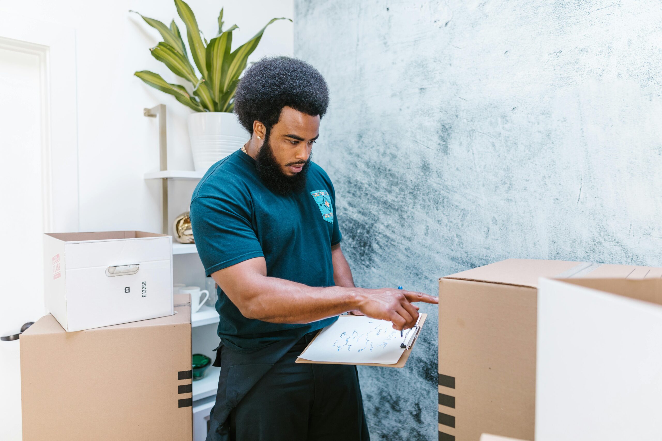 Mover checking inventory list while organizing cardboard boxes in a new apartment.